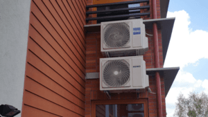 Dwa klimatyzatory zamontowane na czerwonej elewacji budynku.